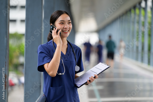 Asian female nurse using phone call in hospital corridor