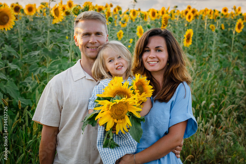 A cheerful young family of father, mother and little daughter in sunflowers field at sunset in the evening