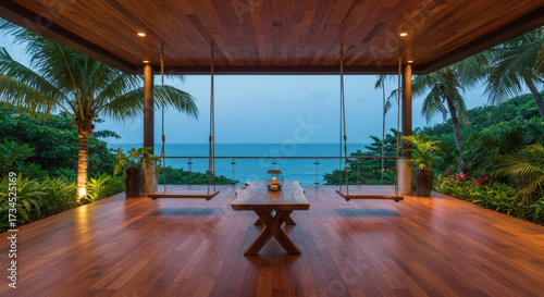 A spacious terrace with an ocean view, wooden flooring, swings and a wooden table, surrounded by plants and soft lighting