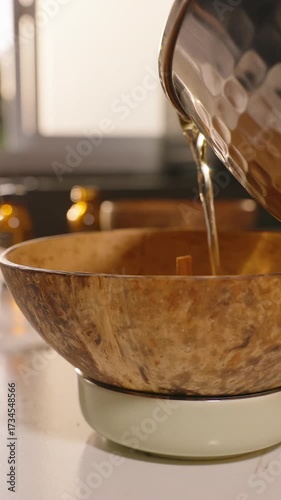 Vertical video. Melted Wax Being Poured From Silver Pot Into Coconut Bowl With Wooden Wick Slow Motion, Homemade Candle Making Concept