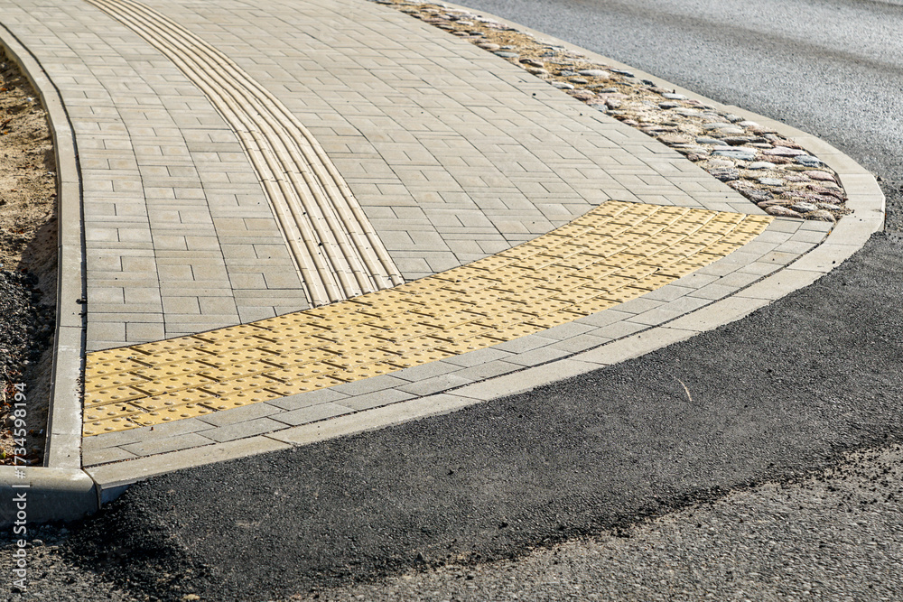 Fototapeta premium Urban sidewalk with tactile paving and guidance strips for accessibility at pedestrian crossing