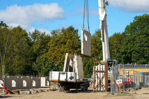 Crane lifting prefabricated concrete wall panels at construction site with workers and equipment