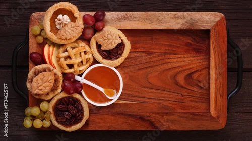 Autumn pie theme dessert board. Top down view stop motion placement video over a dark wood background. Pumpkin, apple and pecan mini pies, with whipped cream, caramel and fruit.