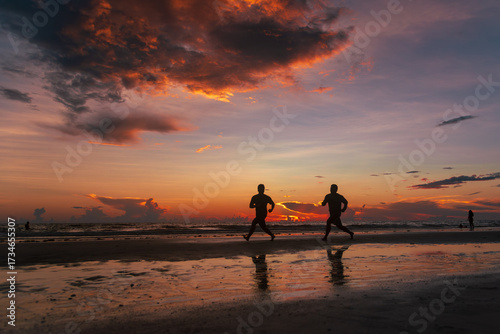 Silhouettes of two men running along a beach at sunset