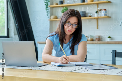 Young serious woman working with laptop sitting at table at home