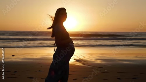 Silhouette of a pregnant woman standing on the beach at sunset, with waves gently lapping in the background