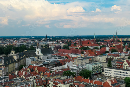 Historic churches and colorful rooftops fill the cityscape of Wroclaw, Poland, as the bustling urban environment blends tradition and modernity under a vast, cloud-streaked sky.