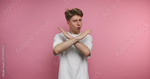 footage of young man is making a no gesture with crossed arms, conveying a sense of disagreement or defiance on pink background