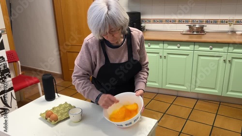 Senior woman with white hair whisking eggs to make Spanish omelette at home