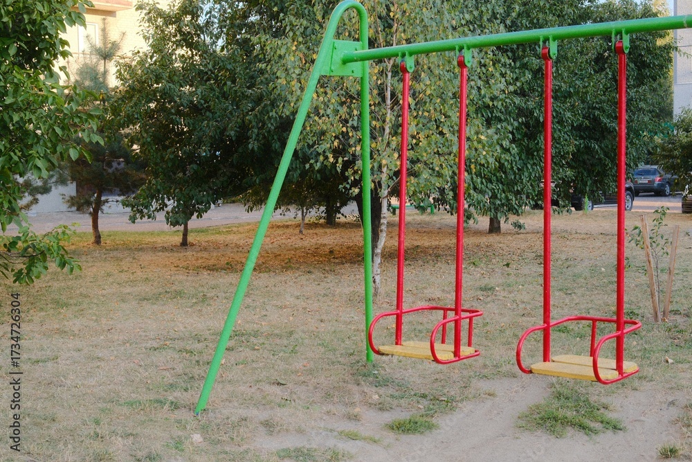 Fototapeta premium Two swings hang still in a public park setting during daytime.