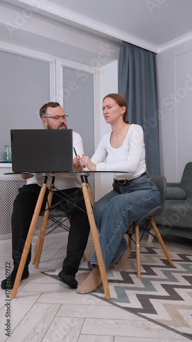 Professional colleagues collaborating at small table, working together on laptop in home office setting with focused communication and shared productivity vertical video