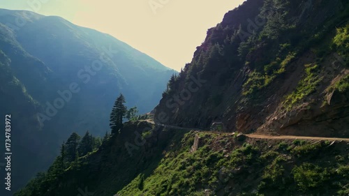Curving Mountain Road Carved into Steep Green Hillside Under Blue Sky — Remote Wilderness Travel Route Through Rugged Terrain in the Himalayas