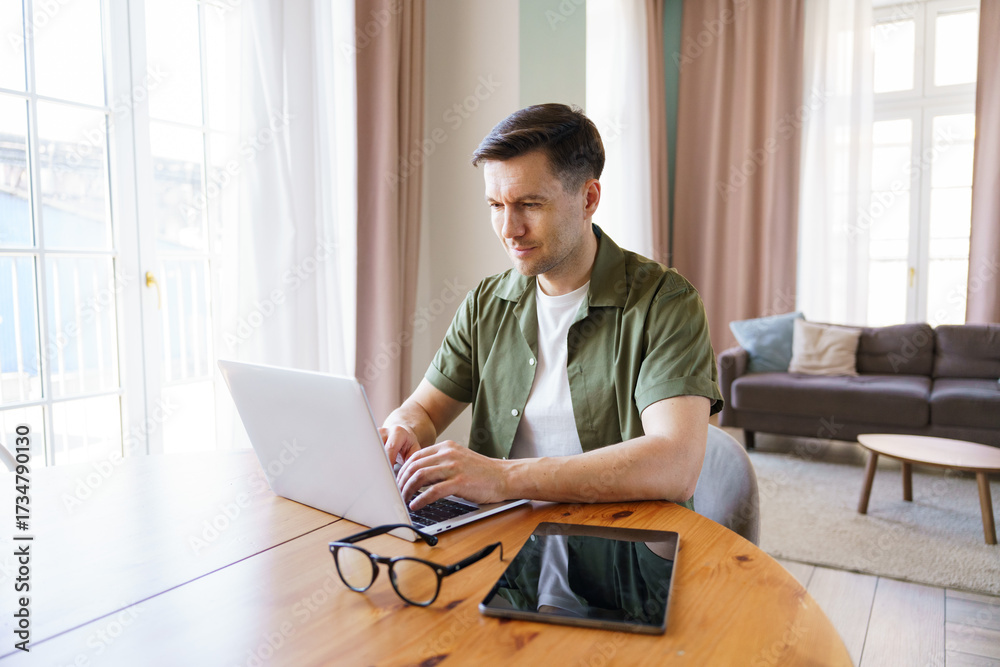 Fototapeta premium Young man works on laptop in cozy living room environment