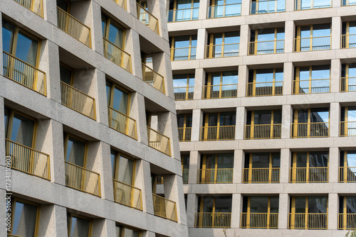 Modern residential apartment building facade with golden yellow balcony railings and geometric concrete architecture pattern. Concept for contemporary housing, urban development. 