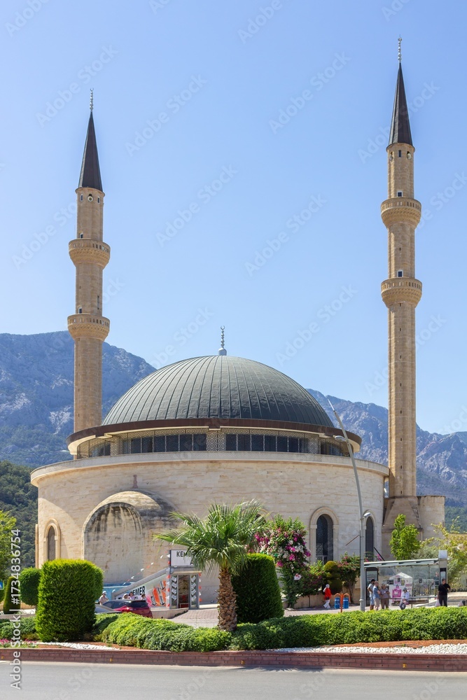 Fototapeta premium Kemer Cami mosque with twin minarets in Kemer city center, Antalya Province, Türkiye, against mountain landscape and clear blue sky
