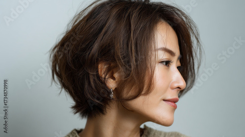Side portrait captures Japanese woman with short brown hair and an earring against a plain background