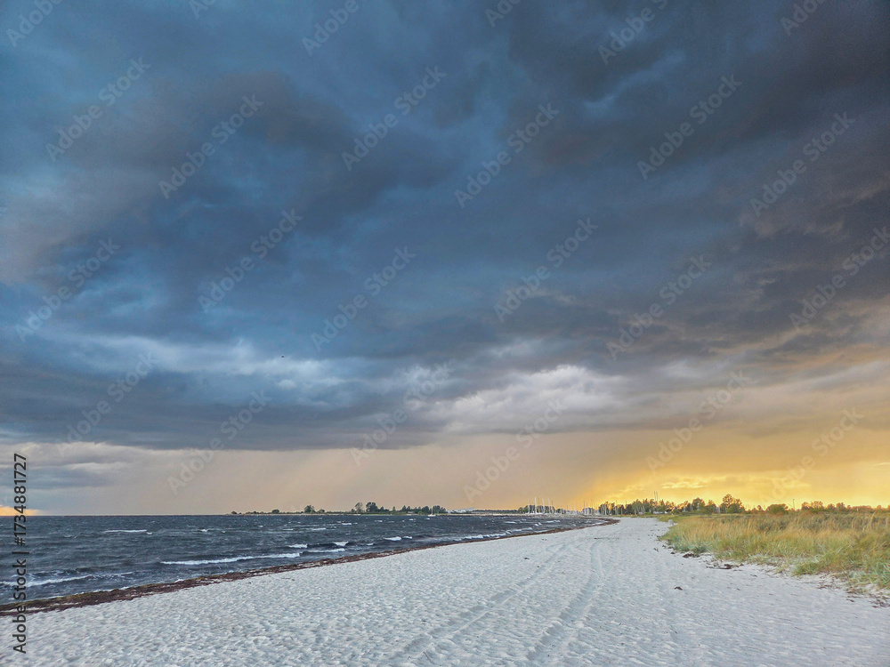 Fototapeta premium Denmark - Dramatic cloudy skies with golden light over a tranquil sandy beach and ocean at dusk