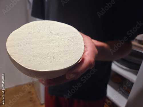 Εκτύπωση καμβά A hand holds a large, circular cross-section of a Giant Puffball mushroom (Calvatia gigantea), revealing its smooth, dense, white edible flesh against a dark, indoor background