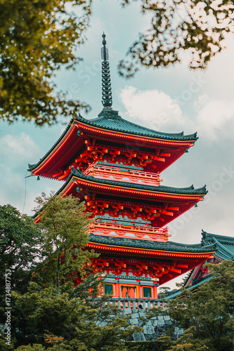 Kyoto, Japan: Kiyomizu-dera Temple red pagoda (Sanjū-no-tō) framed by trees. Vermillion Buddhist architecture, multi-tiered roof structure, UNESCO site.