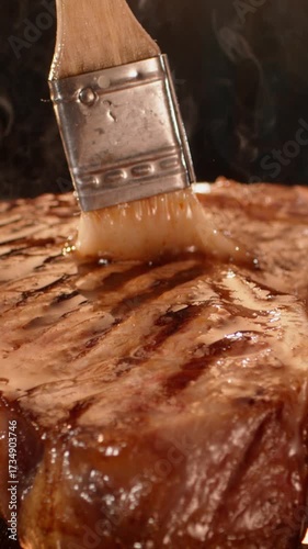 Close-up macro shot of a professional chef applying sauce to a piece of raw red meat with a brush in slow-motion