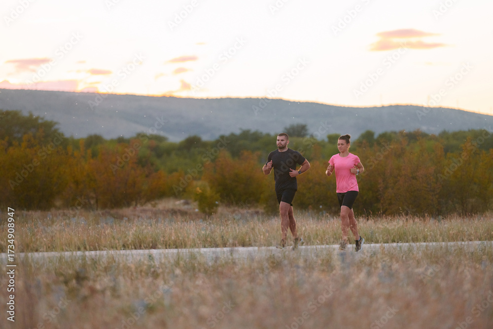 Obraz premium A couple dressed in sportswear runs along a scenic road during an early morning workout, enjoying the fresh air and maintaining a healthy lifestyle