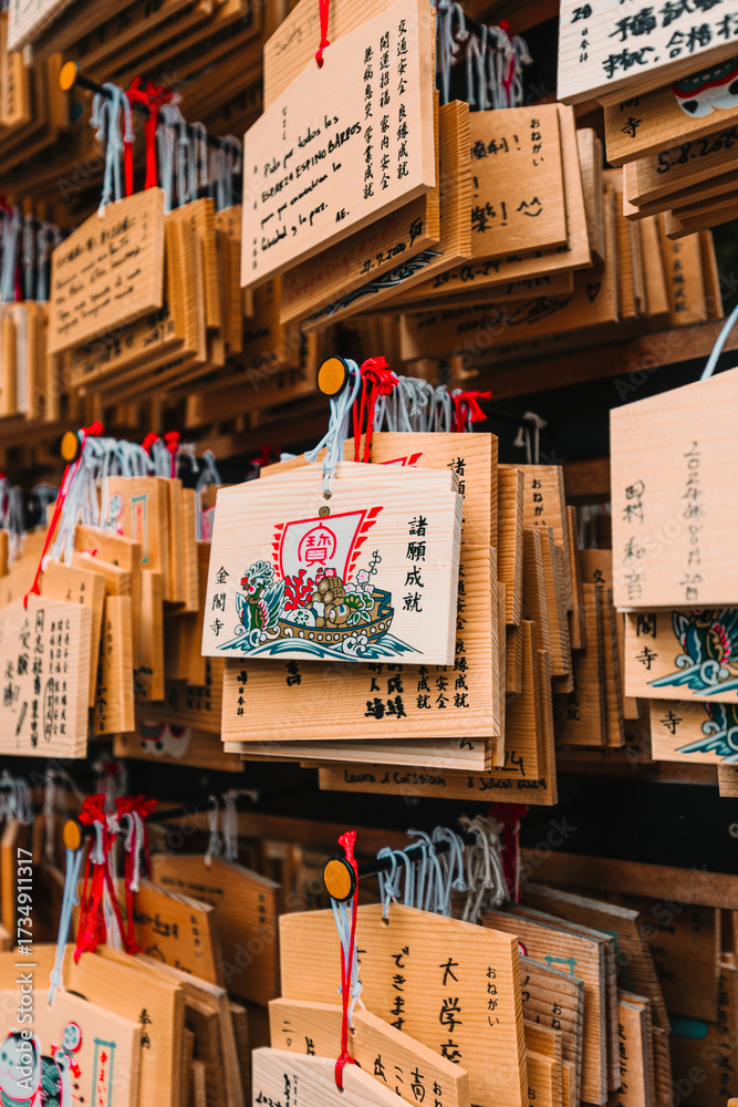 Obraz premium Wooden Ema prayer plaques hanging at a Japanese shrine or temple. Close-up of traditional wooden wishing tablets with calligraphy and red ties.