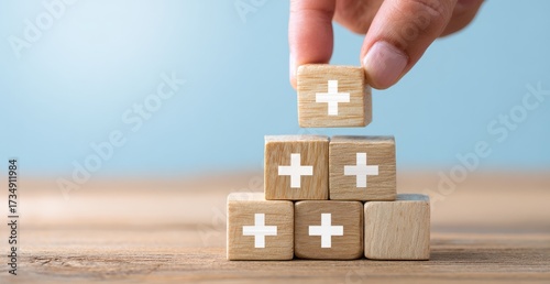 Wooden blocks with plus signs being stacked,  a hand places another block on top