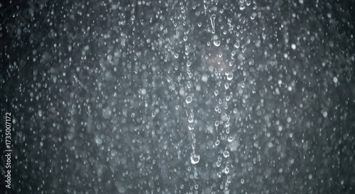 Water droplets against a dark background.  Clusters of small, round water droplets, varying in size, fall and cling to a surface.  A dark gray backdrop enhances the droplets' visibility