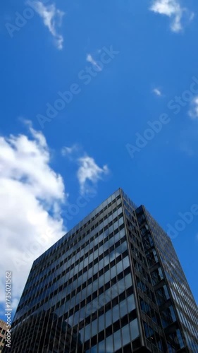 Low-angle view of a modern glass skyscraper reflecting a vibrant, cloudy blue sky on a sunny day
