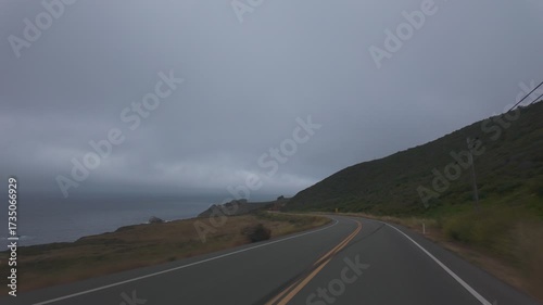 Big Sur California USA video footage driving along Highway 1 with coastal road view, yellow curve sign and dramatic clouds over the Pacific Ocean, scenic drive in motion