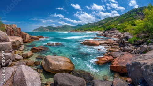 Panoramic coastal view with turquoise water, rocky shoreline, lush green hills, blue sky, and white clouds, evoking tranquility and adventure