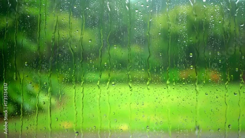 Gentle rain streaks down a window pane, blurring the soft green garden background with a shallow depth of field and a subtle push-in camera movement push-in camera, advertising, rainfall