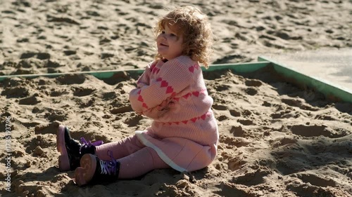 Child playing in sandy area wearing warm sweater on a bright sunny day outdoors