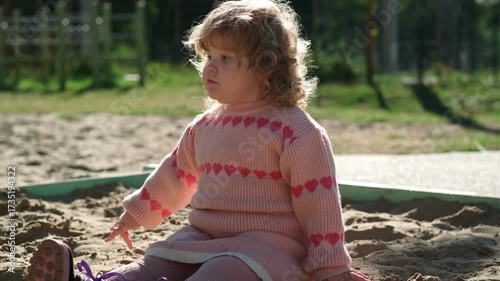 Child playing in sandy area wearing warm sweater on a bright sunny day outdoors