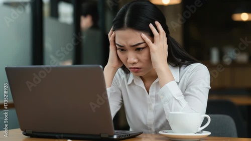 Young woman looking stressed while working on her laptop at a cafe