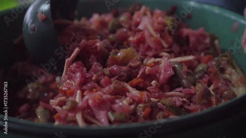 Close-up of a ladle mixing artisanal curtido inside a green pot. Concept of rustic cooking, Central American typical dish, and fresh homemade food.
