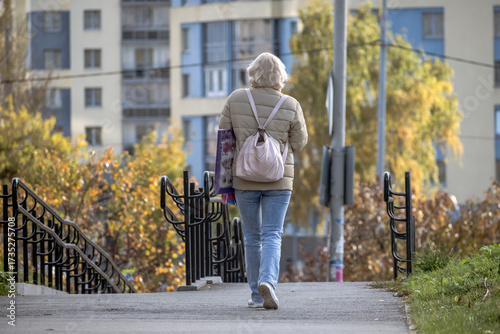 A woman with a backpack walks along the sidewalk on an autumn day