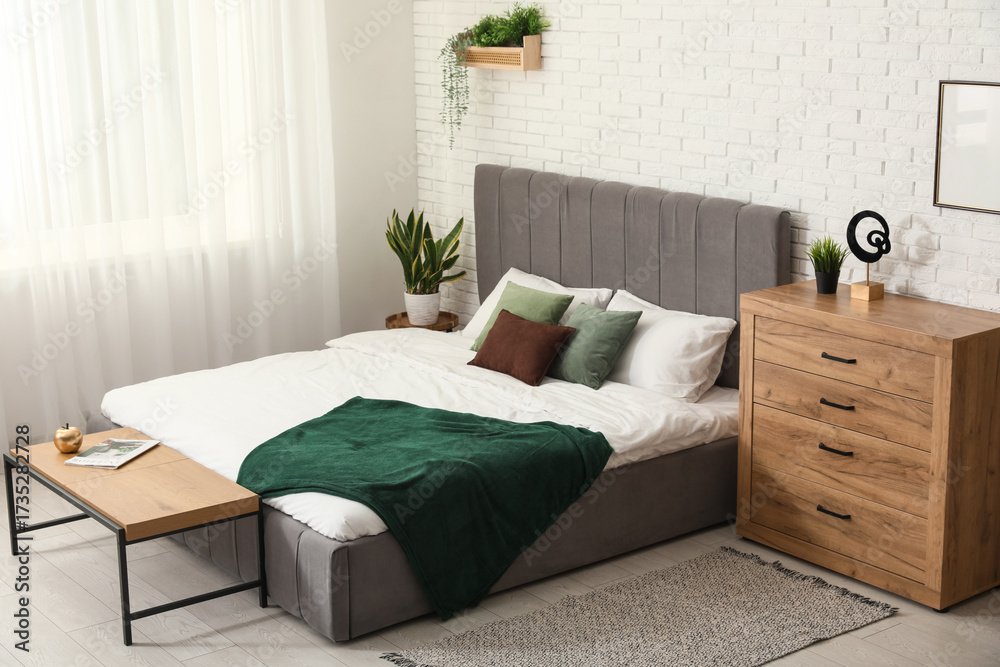 Obraz premium Comfortable bed and chest of drawers near white brick wall in interior of bedroom