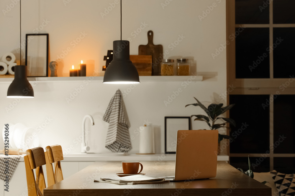 Fototapeta premium Laptop with coffee cup on table in kitchen at night