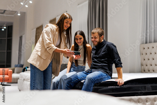Salesperson showing mattress options on smartphone to couple