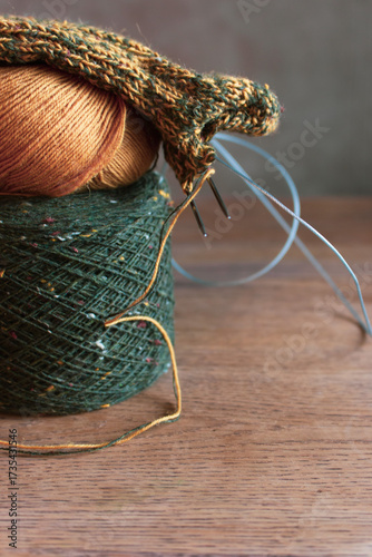 Cozy knitted socks with yarn ball and knitting needles. Knitting process of wool socks. Cozy autumn vibes. Yellow and green tweed yarn on wooden table. Knitting hobby. Knitwear concept. 