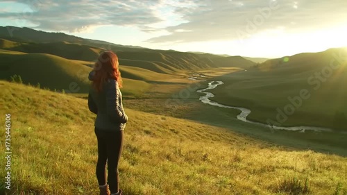 Woman on a hilltop overlooking a river valley at sunset with golden sunlight