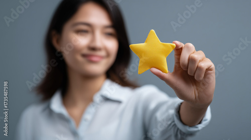 Smiling young woman holding a bright yellow star-shaped object against a soft gray background, symbolizing achievement and creativity