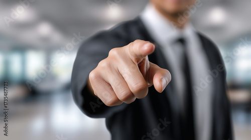 Focused Businessman Pointing at the Viewer with Blurred Office Background in Professional Setting, Symbolizing Leadership and Authority in the Workplace