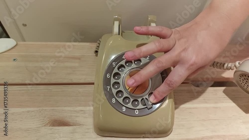 Close-up video of a hand dialing numbers on a classic rotary telephone. The vintage device with a circular dial represents retro communication, nostalgia, and old technology.