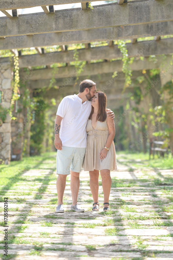 Fototapeta premium A man and woman are kissing in a garden. The woman is wearing a dress and the man is wearing shorts