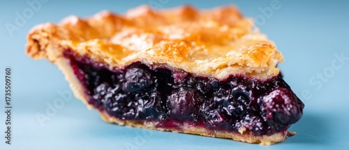 Delicious homemade blueberry pie slice with golden crust and vibrant purple filling on light blue background