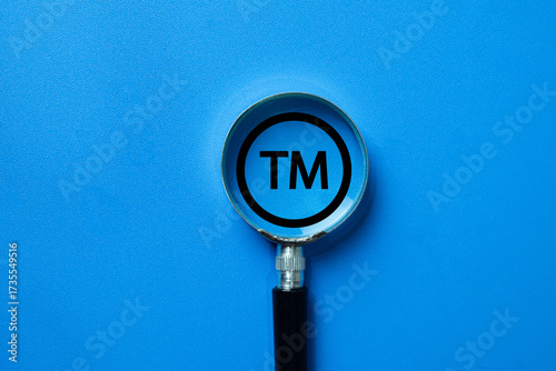 A magnifying glass focusing on a Trademark (TM) symbol. A concept for intellectual property (IP) law, brand protection, and the process of registering a name, logo, or slogan.