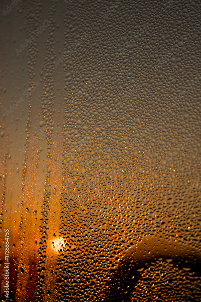 Obraz premium water droplets from condensation on the window glass at sunset, wet glass with water droplets on the background of an orange sky out of focus at sunset