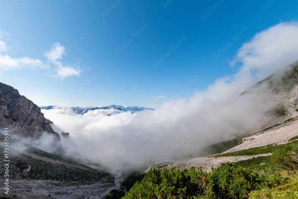 Obraz premium Cloud inversion drifting through rugged alpine landscape under clear blue sky